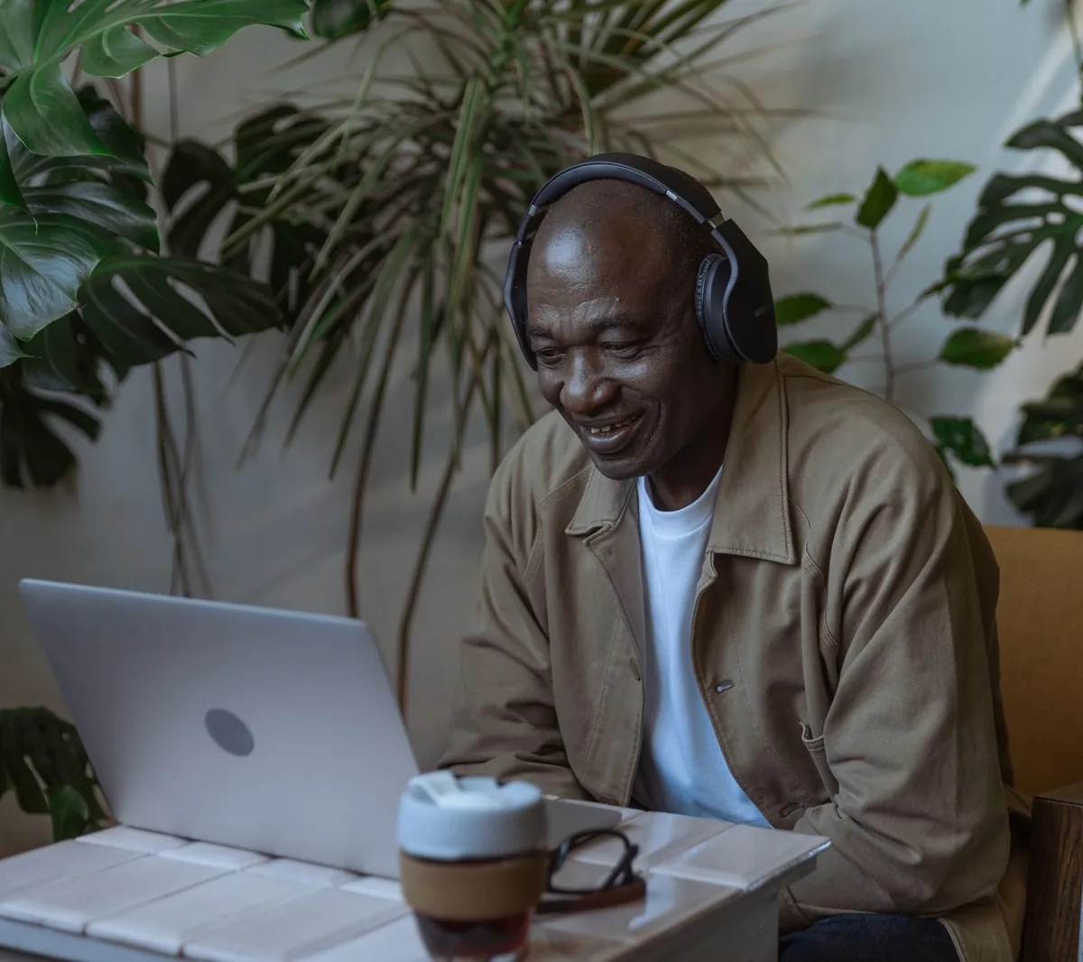 Older man wearing headphones smiling at his laptop at home