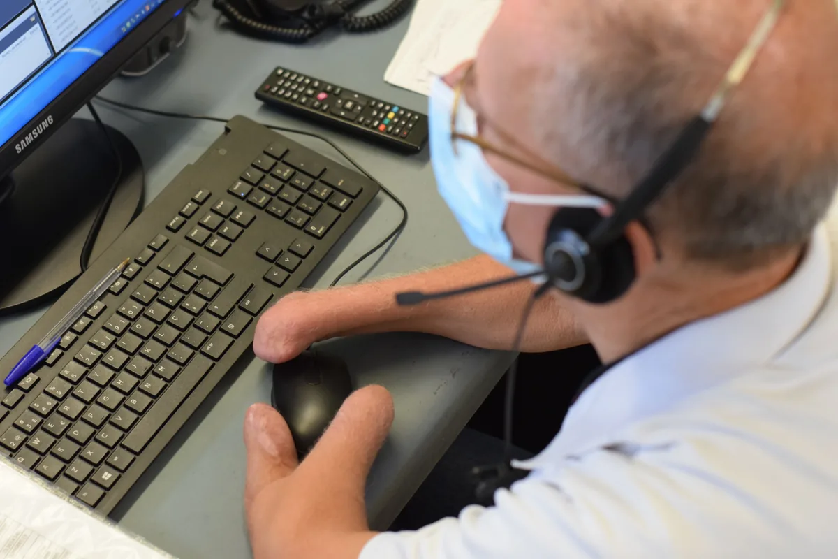 Man with limited hand dexterity wearing a headset microphone, using a mouse at his desk