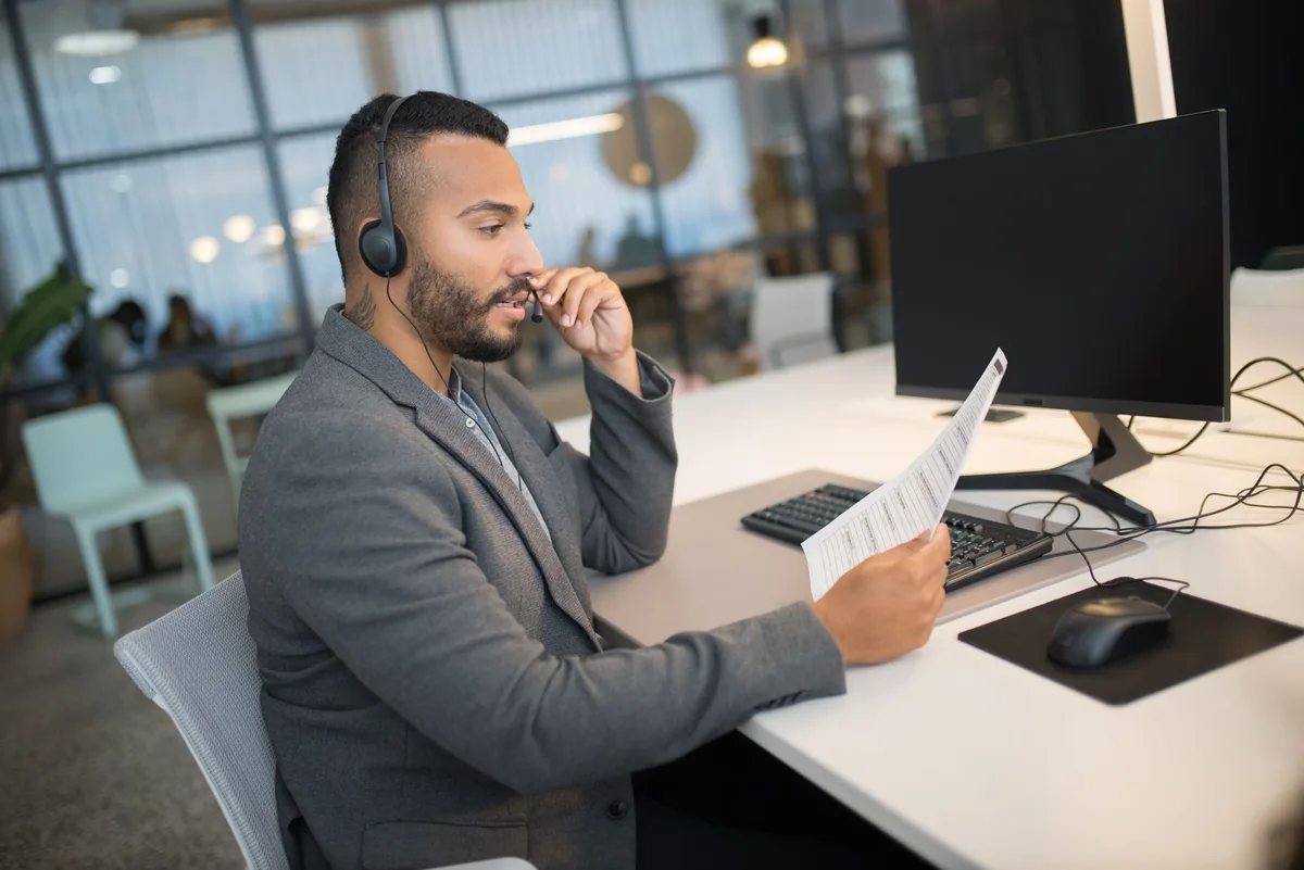 Office coordinator with a headset reading a printed form at his desk