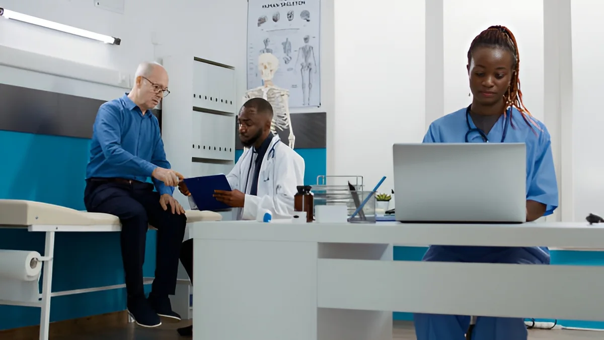 Clinician typing while a doctor speaks with a patient in an exam room