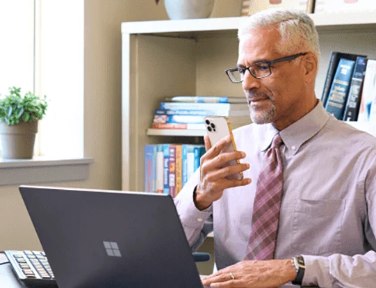 Physician dictating into a phone at his desk beside a laptop